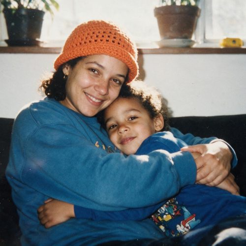 A mother in an orange knit hat hugging her young child on the couch